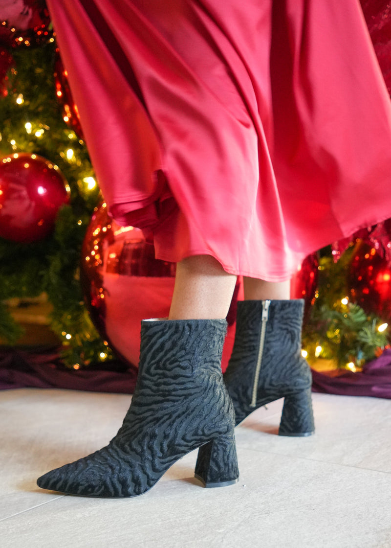 Person wearing black patterned boots with a red skirt in front of a decorated Christmas tree.