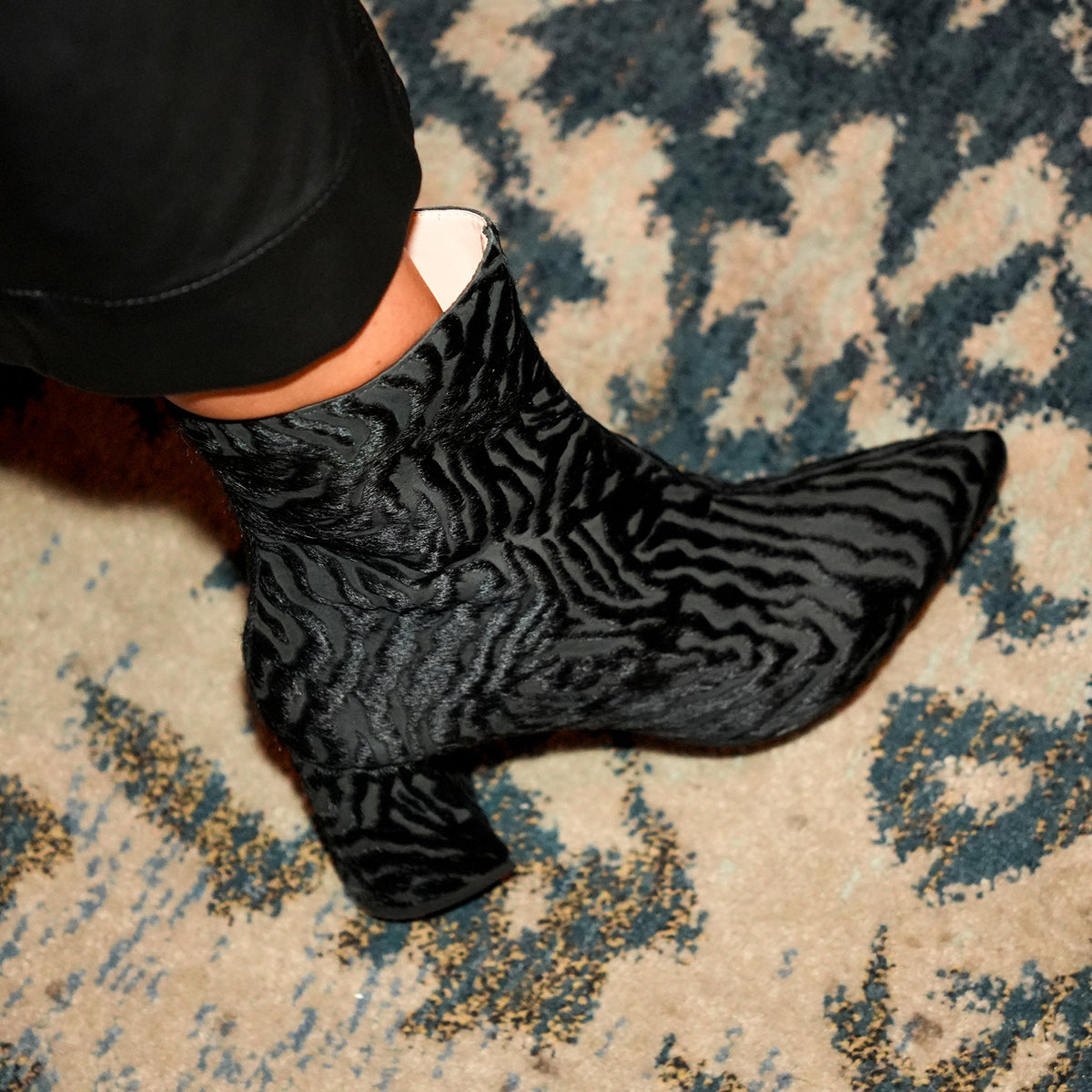 Close-up of an Alterre Hairy Zebra Boot worn with black trousers on a patterned rug.