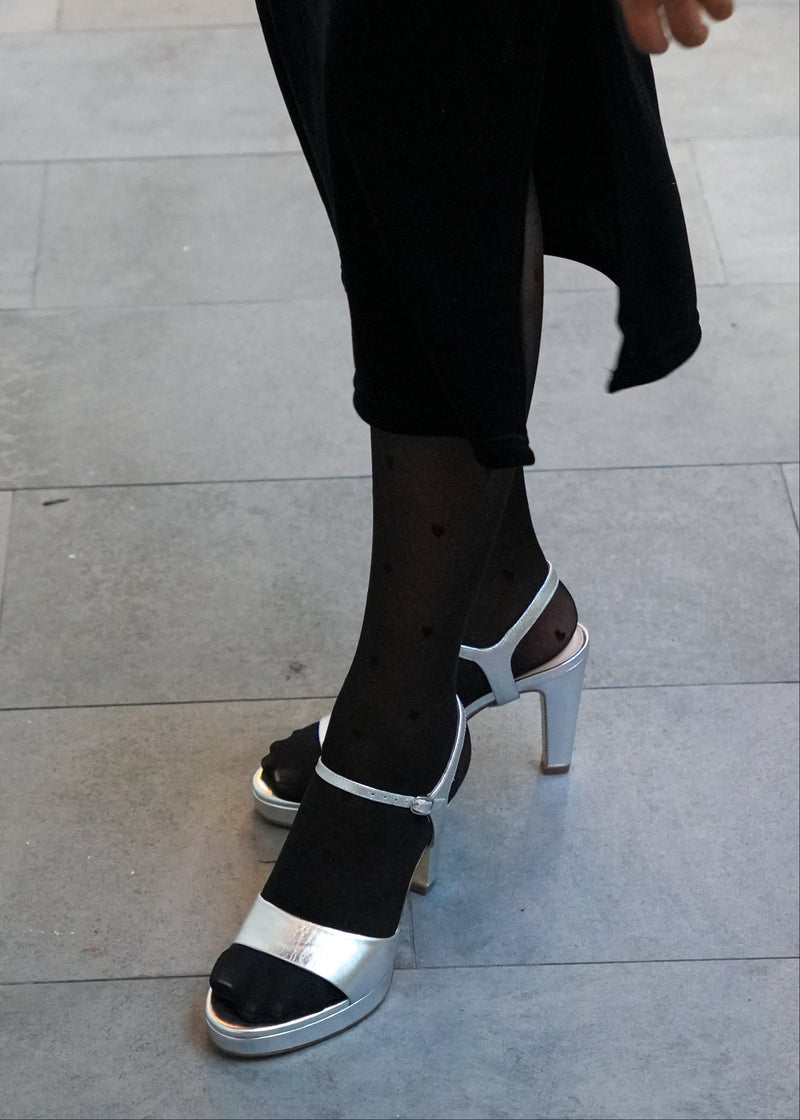 Person wearing silver high-heeled shoes with silver straps on a tiled floor.