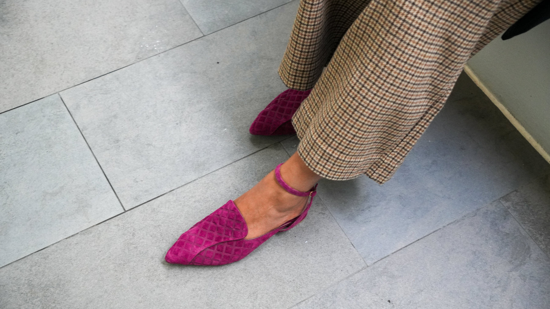 Person wearing purple suede pointed-toe shoes and plaid pants on a gray tiled floor.