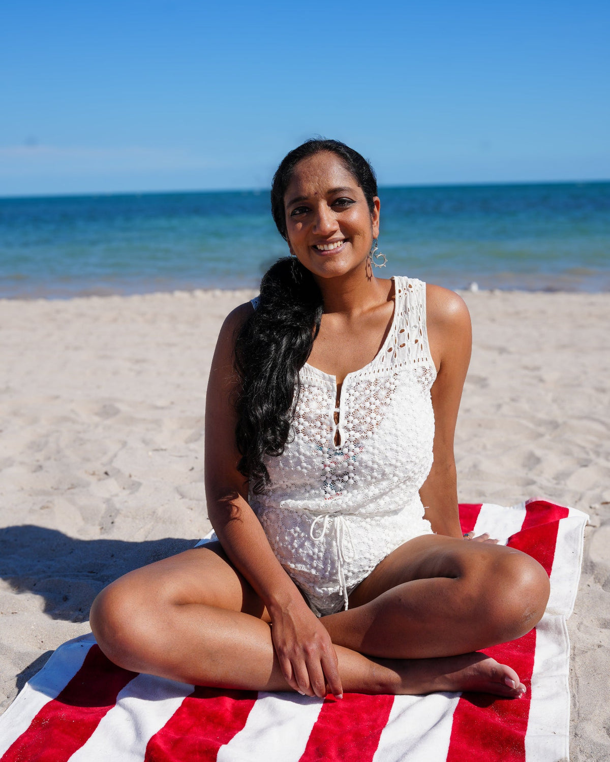 Shilpa, founder of Alterre, sitting on a beach with a blue sky and ocean in the background